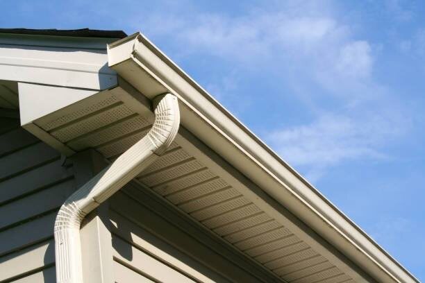 White downspout elbow connecting a gutter to the wall under a vented soffit